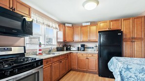 A kitchen with wooden cabinets, a black refrigerator, a microwave, a stove, and a window with blinds. - Beach House 2 Blocks to Beach Free Beach Badges, Towels & Parking (Seaside Heights)