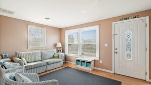 A living room with a striped sofa, wicker chairs, a small table, and a door labeled "HIERING AVE". - Beach House 2 Blocks to Beach Free Beach Badges, Towels & Parking (Seaside Heights)