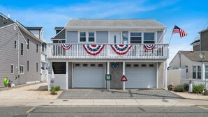 A two-story building with a white facade, a balcony with red, white, and blue decorations, and an American flag on the right. - Beach House 2 Blocks to Beach Free Beach Badges, Towels & Parking (Seaside Heights)