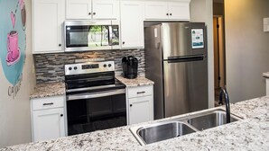 A modern kitchen with white cabinets, a stainless steel refrigerator, a microwave, an oven, and a coffee maker.
