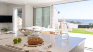 Een moderne keuken met een groot eiland, een brood, twee groene appels, een karaf en een glas water.
