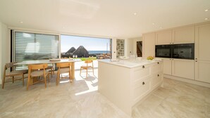 Een moderne keuken met een groot eiland, witte kasten en uitzicht op zee.