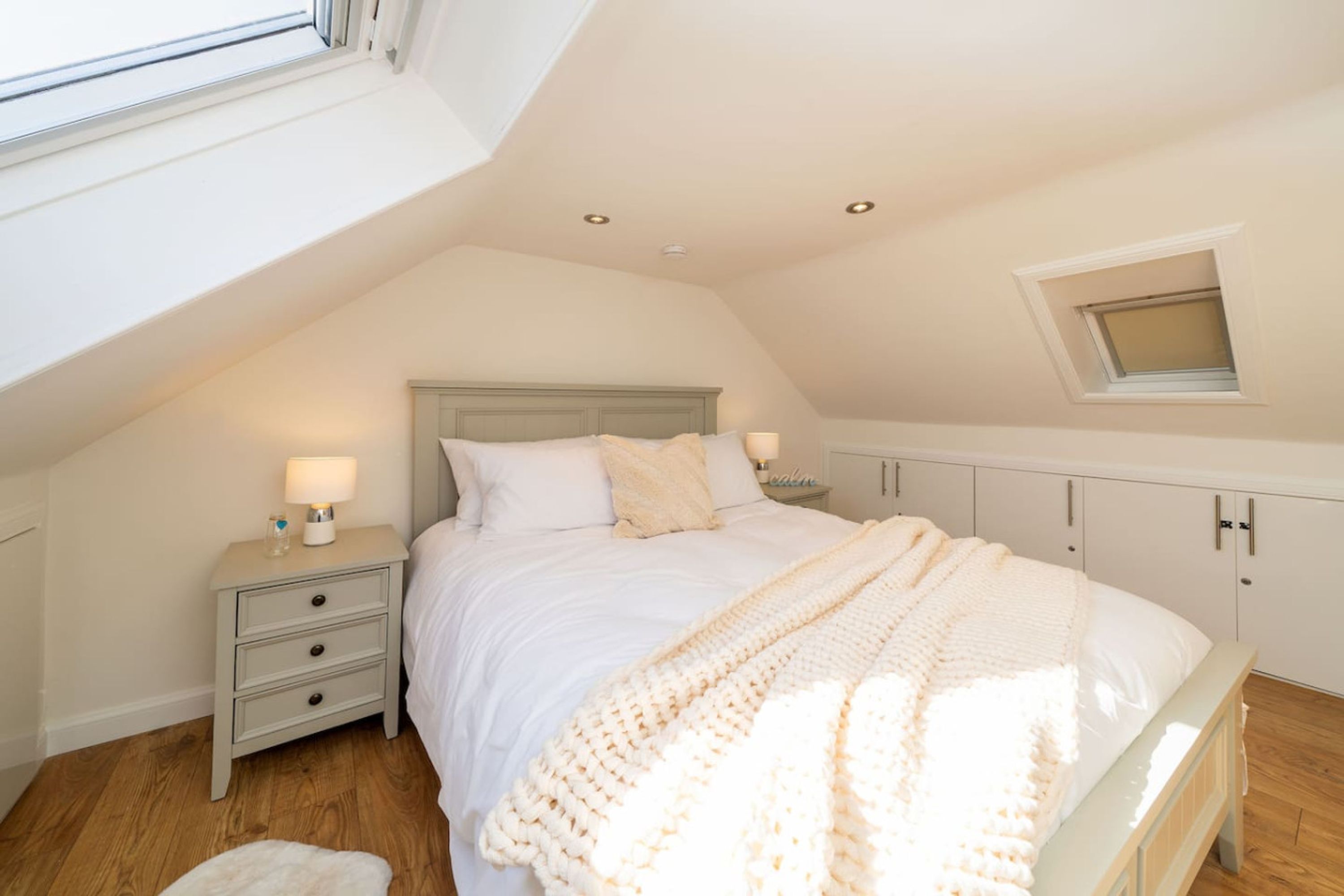 Una camera da letto con soffitto spiovente, un letto con biancheria bianca, un comodino con una lampada e una piccola finestra.