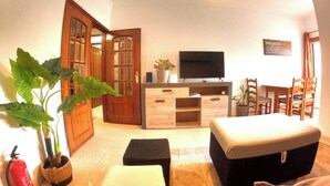 A living room with a TV, wooden furniture, a potted plant, and a fire extinguisher. - Lisbon, modern T2 with balcony in Barcarena (Oeiras)