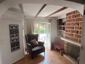 A living room with a dark leather armchair, a decorative metal piece on the wall, a fireplace with a stone facade, and a sliding glass door leading to an outdoor area.
