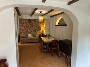 An interior with a dining area, a sofa, a fireplace, and a stone wall.