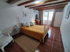 Un dormitorio con cama, una silla, cómoda, espejo y una puerta.