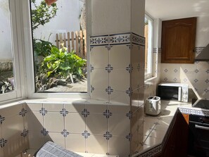 A kitchen with white and blue patterned tiles, a window with a view of greenery, a toaster, and a microwave.