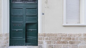 A green door with a decorative top, a window with horizontal blinds, and a stone wall base. - La Galla House | Lecce Selection (Lecce)