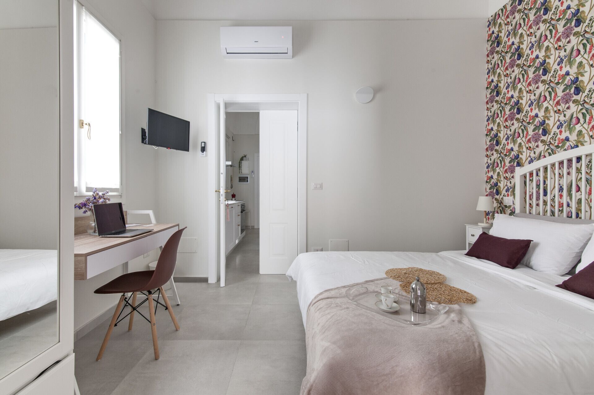 Habitació d'hotel moderna amb llit, escriptori, cadira, televisió i bany visible a través d'una porta oberta.