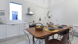 A modern kitchen with white cabinetry, a wooden dining table, and a built-in oven. - La Galla House | Lecce Selection (Lecce)