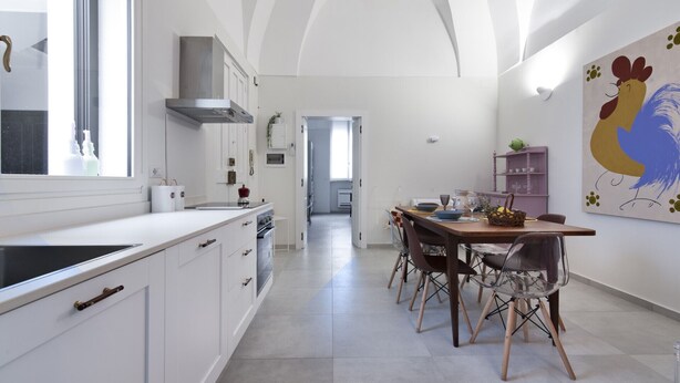 A modern kitchen with white cabinetry, a central island, and a dining area with a wooden table and chairs. - La Galla House | Lecce Selection (Lecce)
