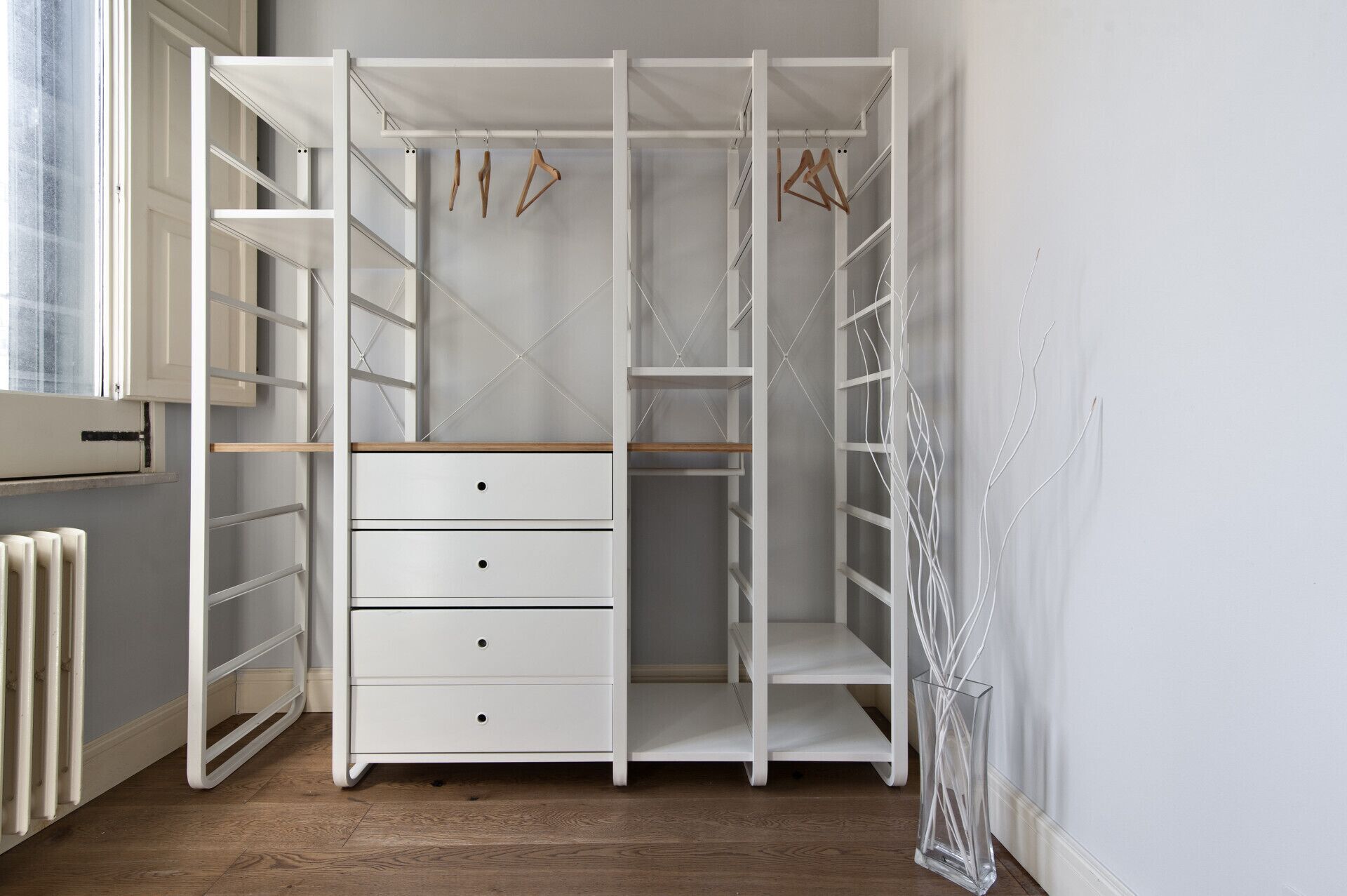A white walk-in closet with open shelving, a wooden bench, and hanging space.