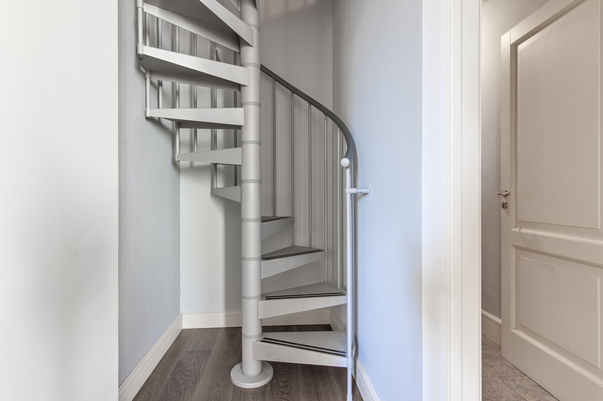 Eine weiße Wendeltreppe mit Geländer und einer Tür am Fuß.