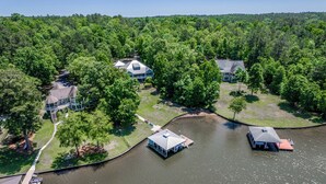An aerial view of a lakeside property with multiple buildings, docks, and a boat. - Lakefront Escape on Lake Sinclair • Hot Tub • Ideal for Families & Friends (Eatonton)