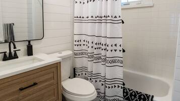 A bathroom with a white toilet, a wooden vanity with a mirror, a black and white patterned shower curtain, and a bathtub.