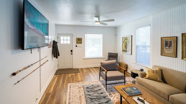 A living room with a flat-screen TV, a ceiling fan, a sofa, a coffee table, and a rug. - Where We Roam Cottage - Walk to Downtown & Lake (Coeur d'Alene)