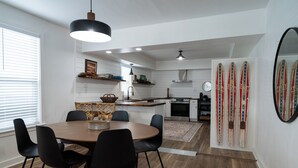 A modern kitchen with white cabinetry, a wooden dining table, black chairs, and a hanging light fixture. - Where We Roam Cottage - Walk to Downtown & Lake (Coeur d'Alene)