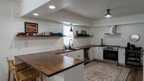 A kitchen with white paneling, wooden countertops, a built-in oven, and a dining area with a wooden table and chairs. - Where We Roam Cottage - Walk to Downtown & Lake (Coeur d'Alene)