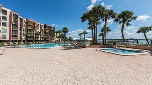 Área de piscina en un complejo turístico con dos piscinas, sillas de descanso, palmeras y vistas al agua.