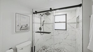 Un baño moderno con ducha envuelta en vidrio, inodoro y suelo de mármol.