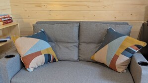A grey sofa with colorful cushions, a wooden wall, and a framed picture above it.