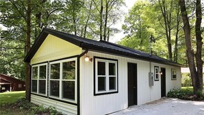 A small, single-story building with a gabled roof and large windows, surrounded by trees. -  The Reel Cottage Leesville Lake No Stairs, firepit, fireplace  NEW WIFI 6/3 (CARROLLTON)