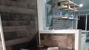 A compact kitchen with a wooden wall, a built-in shelf unit, and a small dining table with chairs. -  The Reel Cottage Leesville Lake No Stairs, firepit, fireplace  NEW WIFI 6/3 (CARROLLTON)