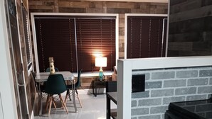 A modern kitchen with a brick accent wall, a dining area with a table and chairs, and a window with blinds. -  The Reel Cottage Leesville Lake No Stairs, firepit, fireplace  NEW WIFI 6/3 (CARROLLTON)