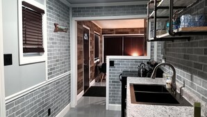 A modern kitchen with a granite countertop, a black sink, and a stainless steel faucet. There is a brick wall with a window and a door leading to another room. -  The Reel Cottage Leesville Lake No Stairs, firepit, fireplace  NEW WIFI 6/3 (CARROLLTON)