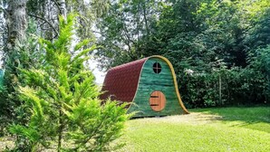Une petite construction verte, ressemblant à une maison, avec un toit rouge, située dans une zone herbeuse entourée d’arbres.