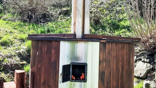 Un sauna en bois doté d’une cheminée, entouré d’une végétation naturelle.