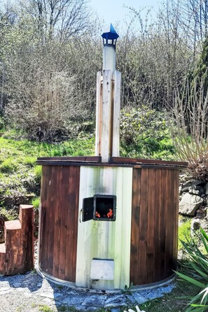 A wooden sauna with a chimney, surrounded by natural vegetation.