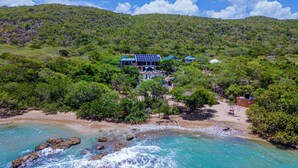 Una propiedad costera con playa, océano y colinas boscosas.