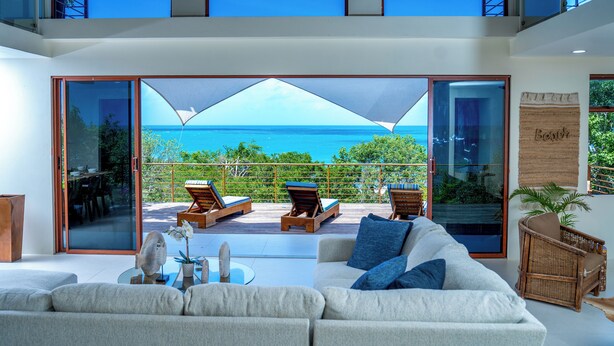 Una sala de estar moderna con un sofá grande, una mesa de centro y vista al océano a través de un ventanal.