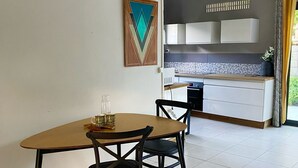 Ein Essbereich mit einem Holztisch und Stühlen, eine Küche im Hintergrund und ein geometrisches Kunstwerk an der Wand.