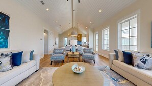 A spacious living room with a high ceiling, a central coffee table, two patterned armchairs, a sofa, and a kitchen in the background. - Shared Resort Style Pools, Boardwalk to the Beach, Beautiful Views (Port Aransas)