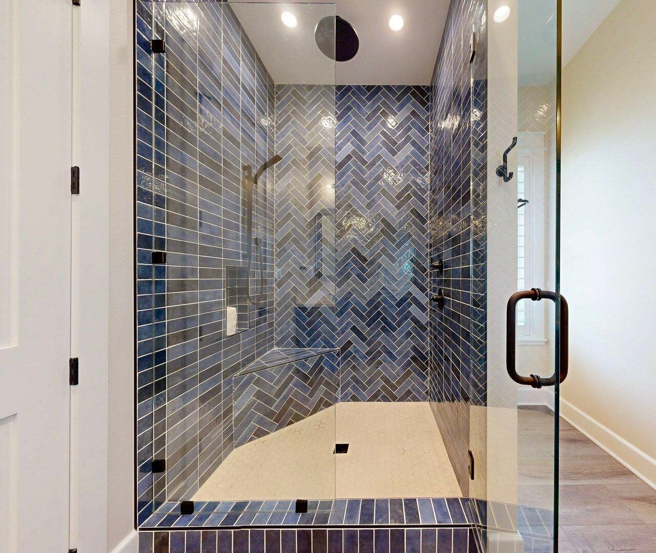 Une douche moderne avec une porte en verre, des carreaux disposés en motif chevron sur les murs et un sol de couleur beige.