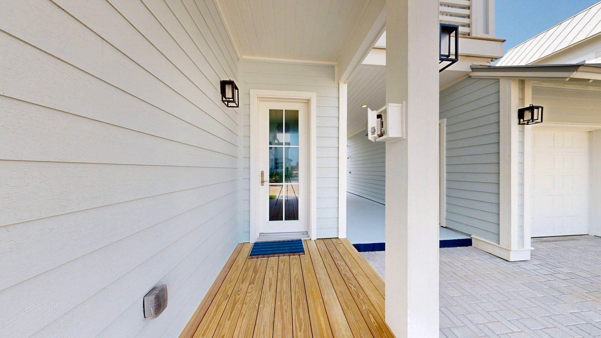 Une véranda couverte avec un plancher en bois, un revêtement extérieur blanc et une porte vitrée donnant sur un garage.