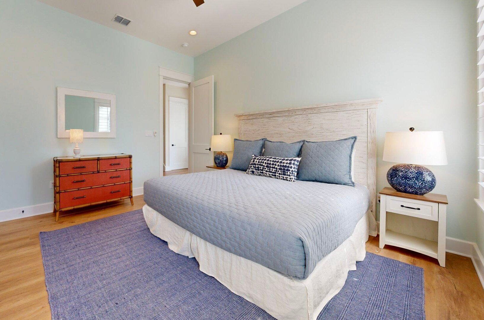 A bedroom with a bed, a dresser, a nightstand, and a lamp.