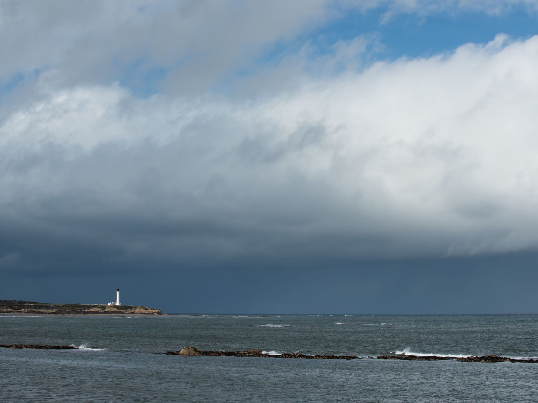 A lighthouse on a rocky coastline with overcast skies.