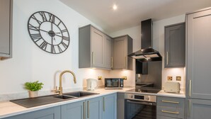 A modern kitchen with grey cabinets, a black clock, stainless steel appliances, and a wooden floor.