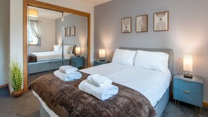 A modern hotel room with a large bed, a mirror, bedside tables, and artwork on the wall.