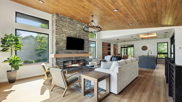 A modern living room with a stone fireplace, wooden ceiling, and large windows. - The Timberline @ Spring Brook Resort (Wisconsin Dells)