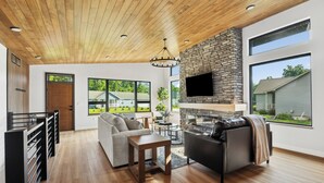 A spacious living area with a stone fireplace, wooden ceiling, and large windows offering a view of the outdoors. - The Timberline @ Spring Brook Resort (Wisconsin Dells)