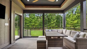 A covered outdoor area with a dining table and sofa, large windows, and a ceiling fan. - The Timberline @ Spring Brook Resort (Wisconsin Dells)
