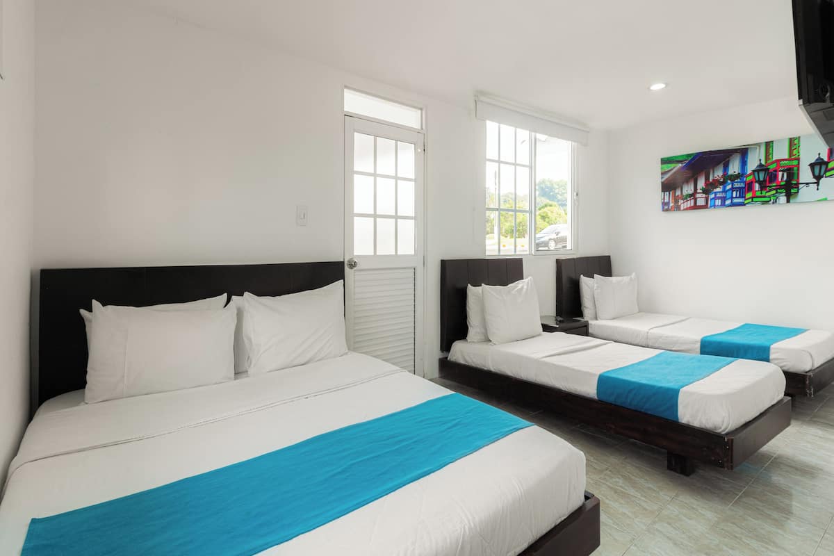 A hotel room with three beds, each with white bedding and blue accents.