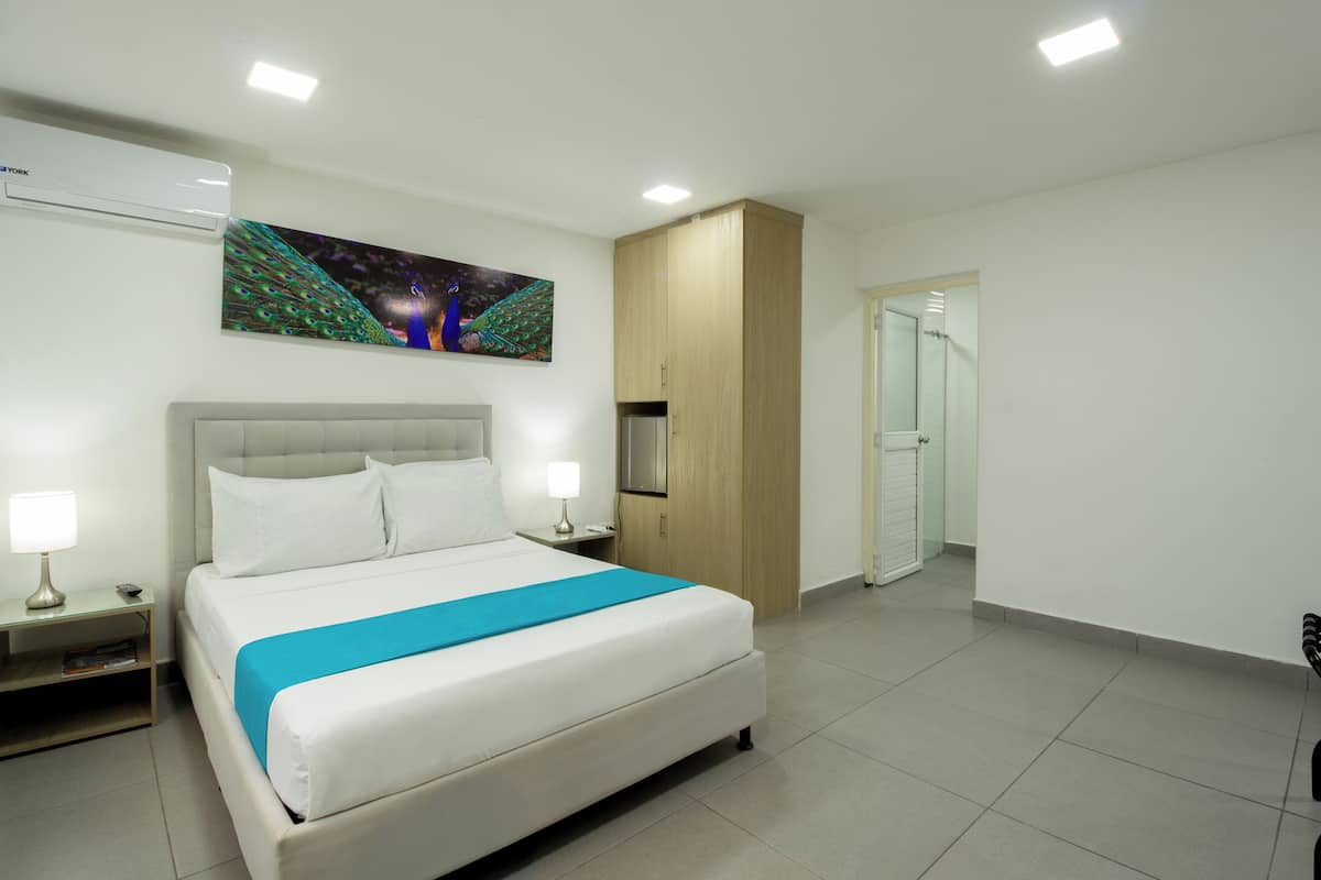 A hotel room with a large bed, a flat-screen TV, a wooden wardrobe, and a door leading to a bathroom.