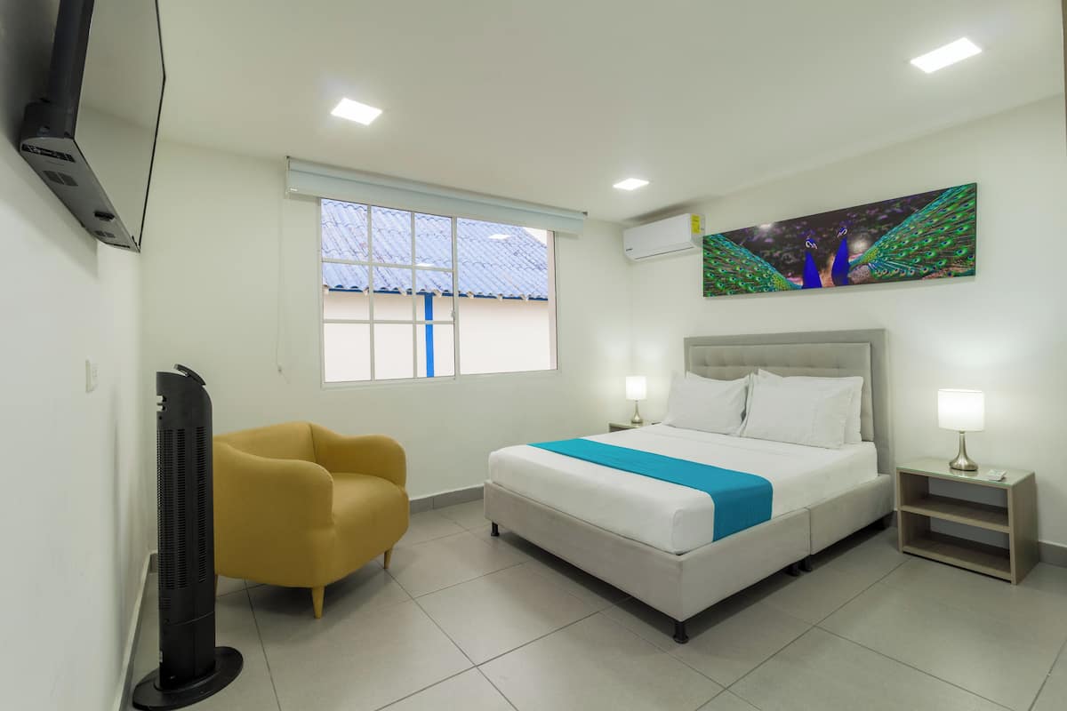 A hotel room with a bed, a chair, a TV, and a painting on the wall.