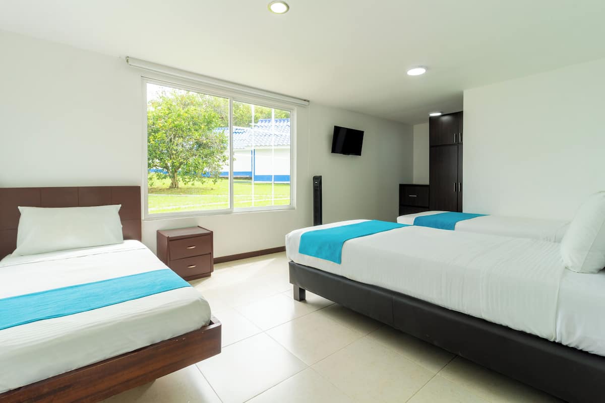 A hotel room with two beds, a TV, and a window with a view of greenery.